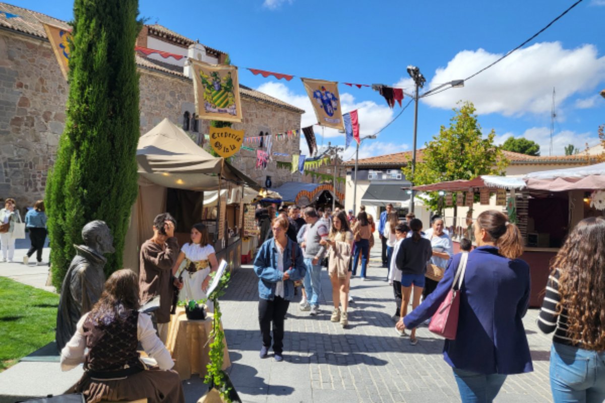 Feira medieval com barracas e bandeiras numa rua de vila histórica