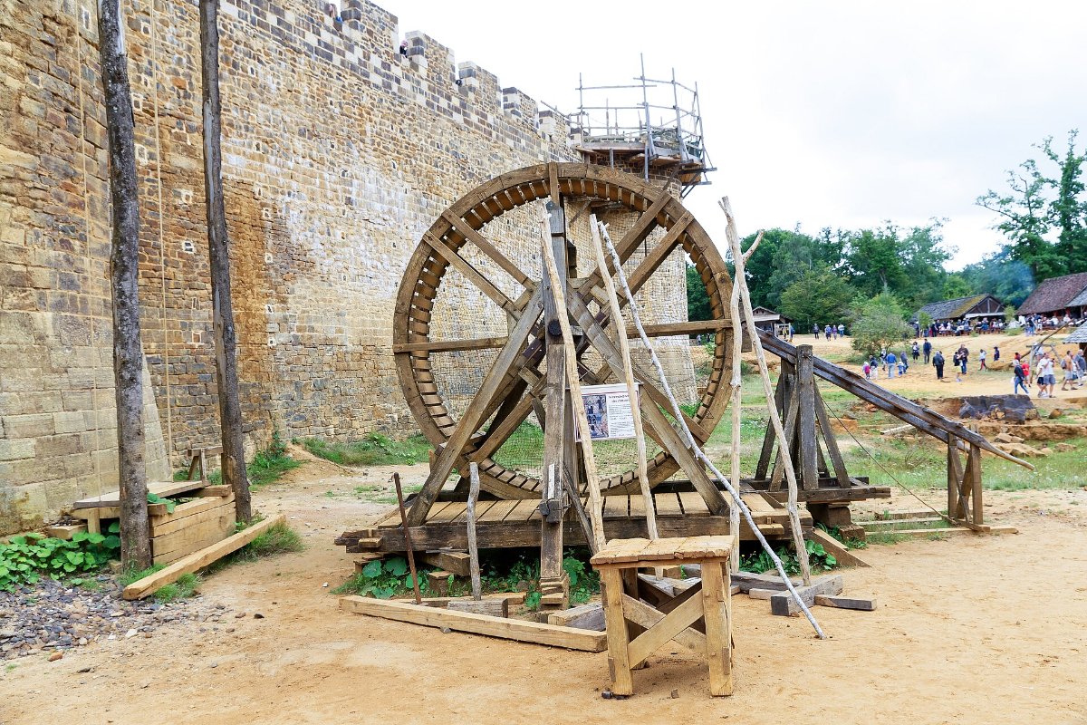 Guindaste medieval de roda de madeira, movido por uma pessoa caminhando dentro dela, junto à muralha de Guédelon